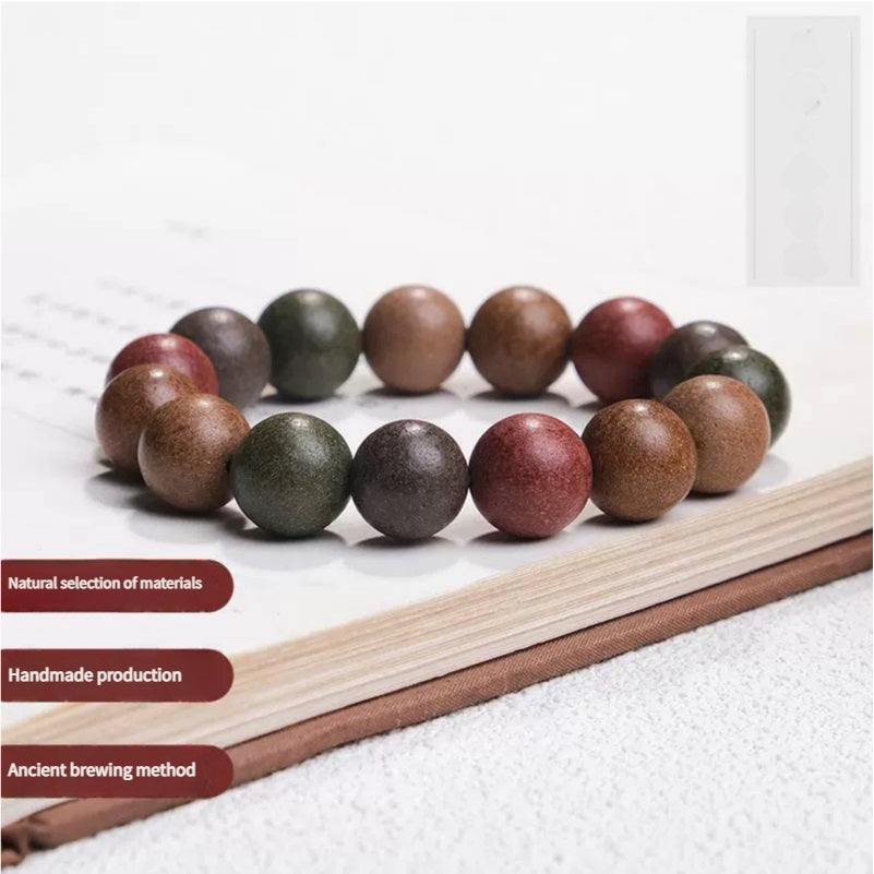 A Chinese Five - Elements Herbal Incense Bead Bracelet placed on a book, with labels indicating natural material selection, handmade production, and ancient brewing method.