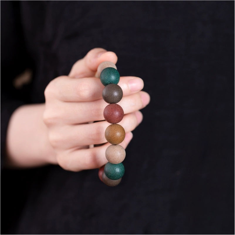 A person's hand holding a Chinese Five - Elements Herbal Incense Bead Bracelet, showcasing the multicolored beads made from traditional Chinese medicine ingredients.
